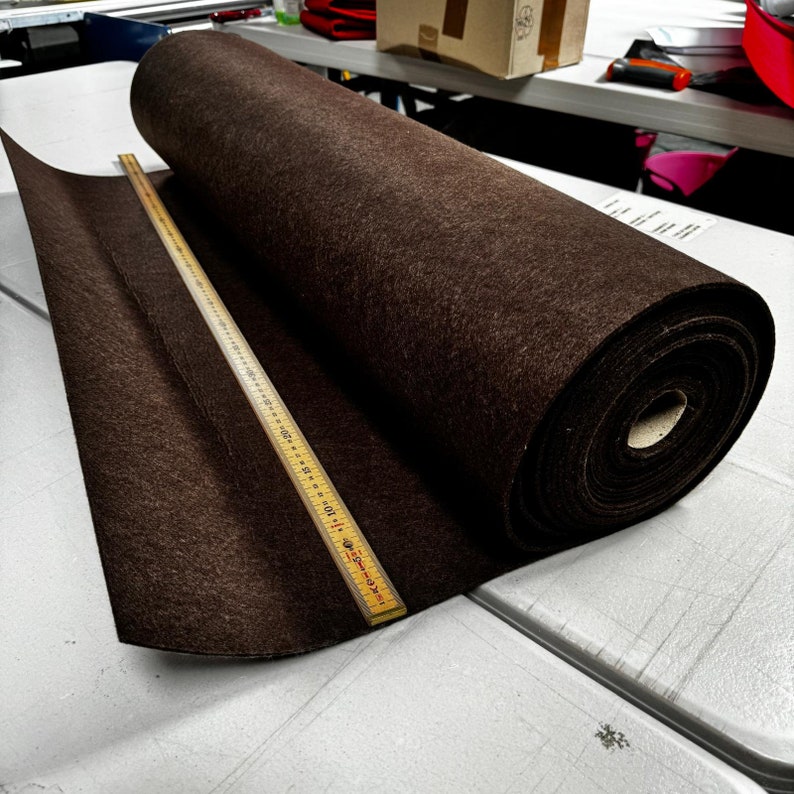 Puede incluir: Un rollo de tela de fieltro marr&oacute;n con una regla de madera que mide 30,5 cm. El fieltro est&aacute; enrollado y el extremo del rollo es visible.
