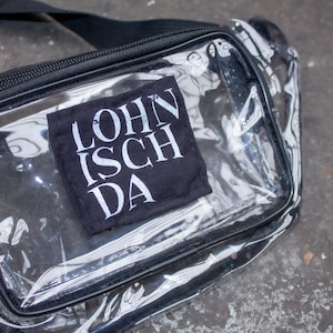 May include: A clear plastic bum bag with a black adjustable strap and a black patch with white text that reads "LOHN ISCH DA".