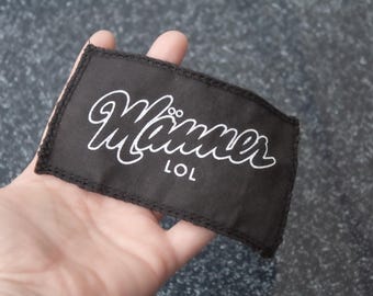 Peut inclure: Patch en tissu noir avec du texte blanc qui dit "Manner LOL".