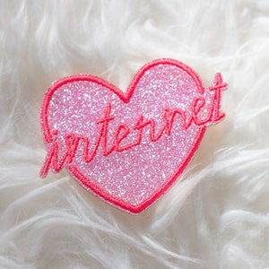 Könnte beinhalten: Rosa glitzernder Herz-Patch mit dem Wort "Internet" in rotem Faden.