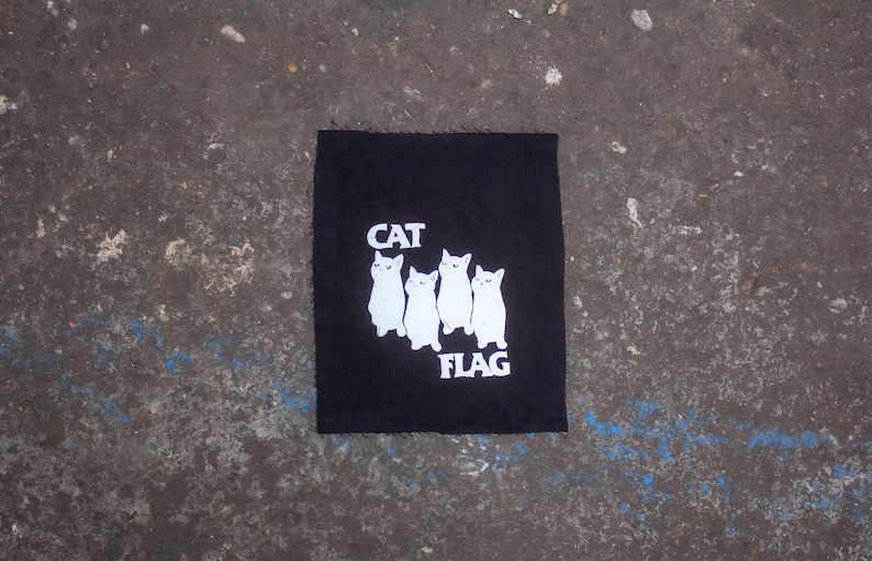 May include: Black fabric patch with white embroidered cats and the text "CAT FLAG".