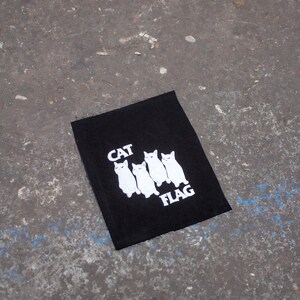 May include: Black fabric patch with white embroidered cats and the text "CAT FLAG".