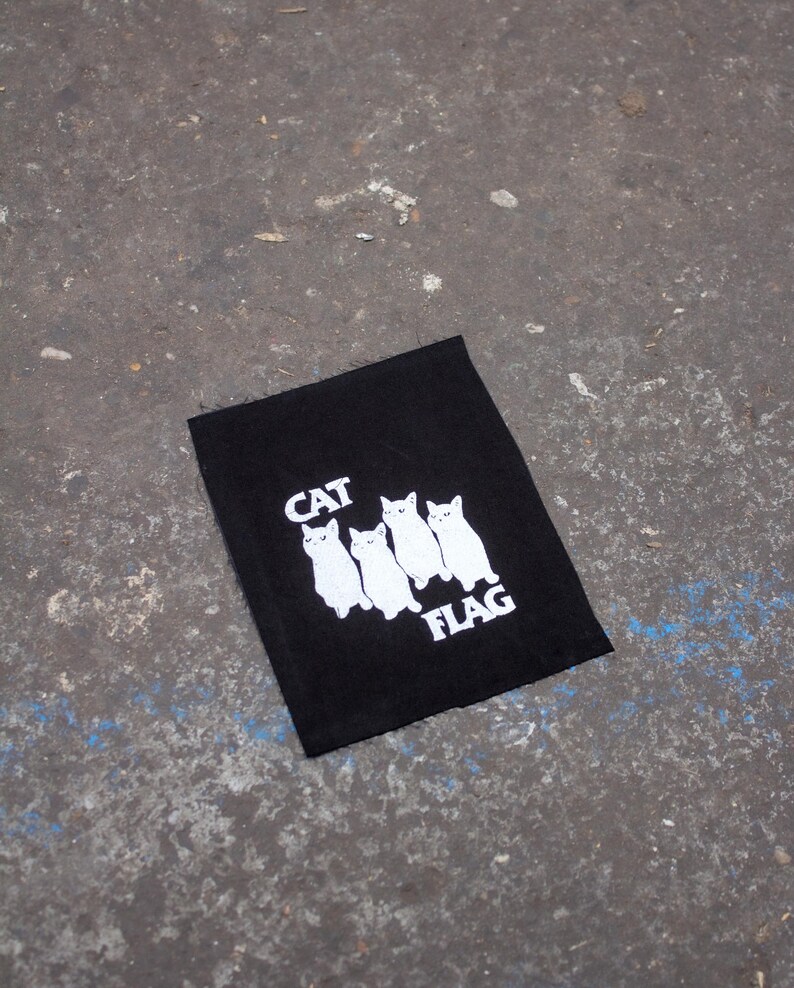 May include: Black fabric patch with white embroidered cats and the text "CAT FLAG".