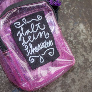 May include: A pink clear plastic bag with a black patch that says "halt dein schnauzem" in white lettering.