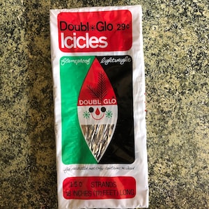 May include: A package of vintage "Doubl Glo Icicles" Christmas decorations. The white package has red, green, and black accents with text that reads "flameproof" and "lightweight". The package contains 150 strands, each 18 inches long.
