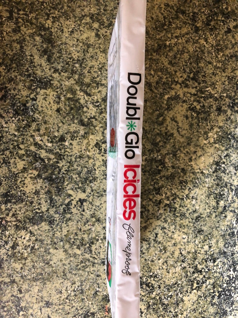 May include: A white package with the words "Double Glo Icicles" in red and black text. The package also has the words "Flameproof" in cursive. The package is on a speckled, brown surface.