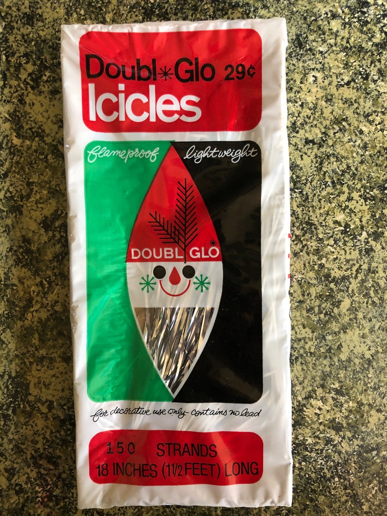 May include: A package of Double Glo Icicles, a vintage Christmas decoration. The package is white with red and green accents, and features the text "Double Glo Icicles" and "150 strands, 18 inches long". The design includes a stylized face.