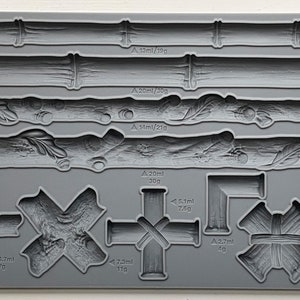 May include: A gray silicone mold with various shapes of faux wood, including logs, branches, and cross-shaped pieces. The mold is labeled "IOD Faux Bois" and includes measurements in milliliters and grams.
