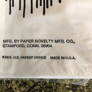 May include: Close-up of a white surface with black vertical lines at the top. Text includes "MFG. BY PAPER NOVELTY MFG. CO., STAMFORD, CONN. 06904" and "*REG. U.S. PATENT OFFICE MADE IN U.S.A."