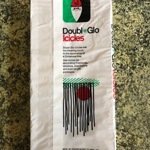 May include: White package of Double Glo Icicles with a green, black, and red logo. The package features text describing the product as a finishing touch for Christmas tree decorations, suitable for fireplaces, windows, and gift packages.