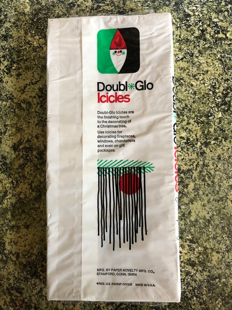 May include: White package of Double Glo Icicles with a green, black, and red logo. The package features text describing the product as a finishing touch for Christmas tree decorations, suitable for fireplaces, windows, and gift packages.