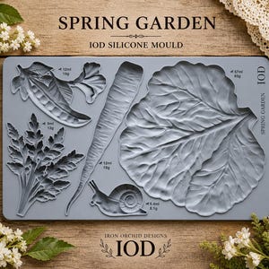 May include: A gray silicone mold with the text "SPRING GARDEN" and "IOD SILICONE MOULD". The mold features detailed vegetable and plant designs, including a pea pod, carrot, leaf, fern, and snail. The Iron Orchid Designs logo is at the bottom.