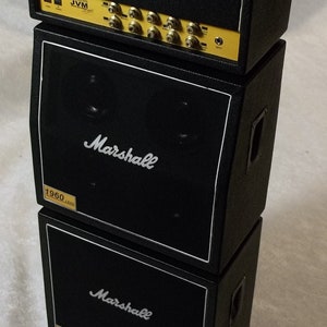 Könnte beinhalten: Ein schwarzer Marshall Gitarrenverstärker-Stack, bestehend aus einem Topteil und zwei Lautsprecherboxen. Das Topteil hat ein gelbes Bedienfeld mit dem Text "JVM" und dem Marshall-Logo. Die Boxen zeigen das Marshall-Logo und den Text "1960 LEAD".