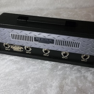 May include: A black Mesa Engineering Single Rectifier Solo Head 50 guitar amplifier head featuring a silver diamond plate metal front panel with five input jacks, a black carrying handle on top, and white text labels for each input port.