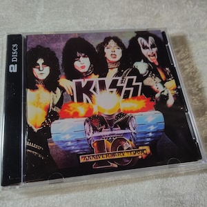 Puede incluir: Una caja de CD con la banda KISS. La portada muestra a los miembros de la banda con maquillaje y disfraces, el nombre de la banda y el texto "10th Anniversary Tour". La caja está etiquetada como "2 DISCS".