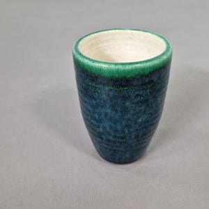 May include: A ceramic tumbler with a textured, blue-green glaze. The rim is a vibrant green, and the interior is a creamy white. This unique piece is perfect for enjoying your favourite beverages.