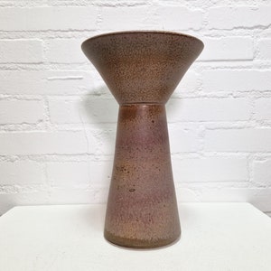 May include: A brown ceramic vase with a wide, flared opening and a narrow base. The vase has a speckled, textured surface.