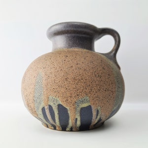 Può includere: Un vaso in ceramica marrone con una glassa macchiata e un designo astratto blu scuro e verde. Il vaso ha un corpo arrotondato e un manico.