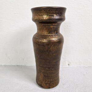 Può includere: Un vaso vintage color bronzo con una superficie strutturata. Il vaso ha un bordo ampio e svasato e un corpo cilindrico che si assottiglia leggermente verso la base. La finitura bronzo presenta variazioni di colore, che aggiungono al suo aspetto antico.