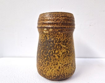 May include: A brown ceramic vase with a speckled glaze. The vase has a rounded body and a slightly flared rim.