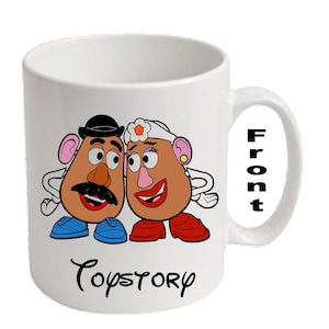 Può includere: Tazza in ceramica bianca con un'immagine a cartoni animati di Mr. e Mrs. Potato Head di Toy Story. La tazza ha un manico nero e la parola "Front" stampata verticalmente sul lato. Le parole "Toy Story" sono stampate in un carattere corsivo in basso.