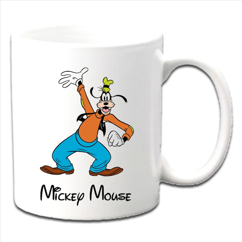 May include: White ceramic mug featuring a cartoon image of Goofy in an orange shirt, blue pants, and brown shoes. The mug has a black "Mickey Mouse" text at the bottom. The handle is white.