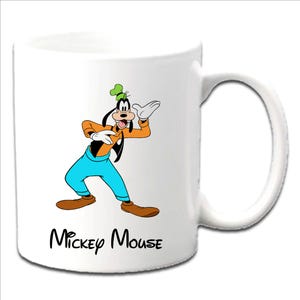 May include: White ceramic mug featuring a colorful illustration of Goofy from Disney's Mickey Mouse. Goofy is depicted in his signature orange shirt, blue pants, and green hat. The words "Mickey Mouse" are printed in black script below the character.
