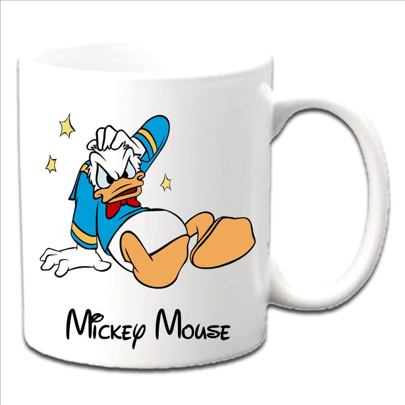 Może przedstawiać: Biały ceramiczny kubek z Kaczorem Donaldem w niebieskiej koszuli marynarskiej, białej pieluszce i pomarańczowych stopach. Kubek ma czarny napis "Mickey Mouse" z ż&oacute;łtymi gwiazdkami.