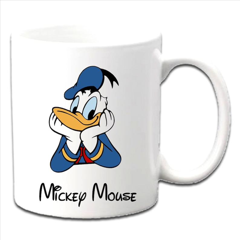 Może przedstawiać: Biały ceramiczny kubek z kresk&oacute;wkowym wizerunkiem Kaczora Donalda w niebieskim stroju marynarza i czapce, z rękami pod brodą. Słowa "Mickey Mouse" są napisane czarnym pismem pod obrazkiem.