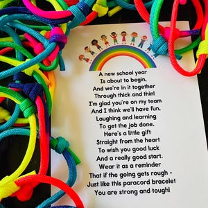 May include: A collection of colorful paracord bracelets in shades of red, yellow, green, blue, and pink. A card with a rainbow and children illustration is next to the bracelets. The card has a poem about a new school year.