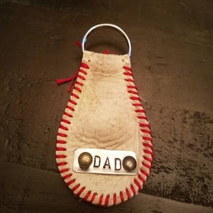 May include: A white baseball-shaped keychain with red stitching and a metal tag that says "DADO".