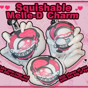 Puede incluir: Un conjunto de tres amuletos de peluche con un personaje de dibujos animados de pelo rojo, que lleva gafas y una gargantilla negra. Los amuletos son blancos con contornos negros y están unidos a llaveros. El texto "Squishable Melle-D Charm" está en la parte superior de la imagen. El texto "Take your rage out on the octoclops!" está en la parte inferior izquierda de la imagen. El texto "Still stares at you with her big ol eye" está en la parte inferior derecha de la imagen.