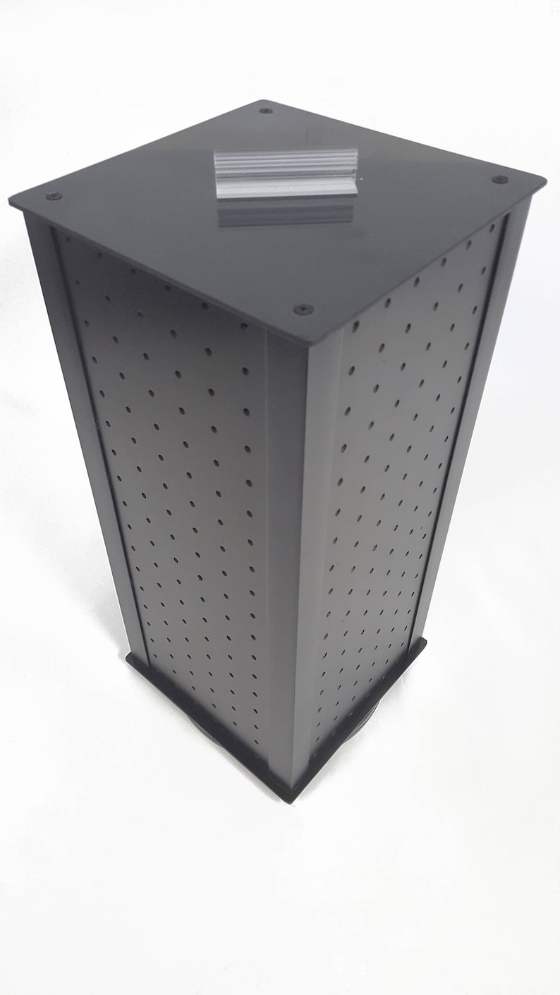 May include: A black rotating display stand with a square base and a perforated surface. The stand is designed for displaying small items, such as jewelry or accessories.