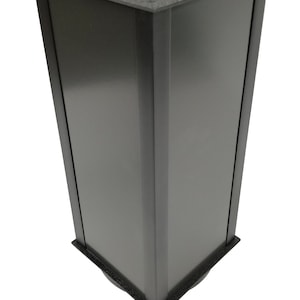 May include: A black square trash can with a rectangular opening on the top. The trash can has a black rubber trim around the top and bottom.