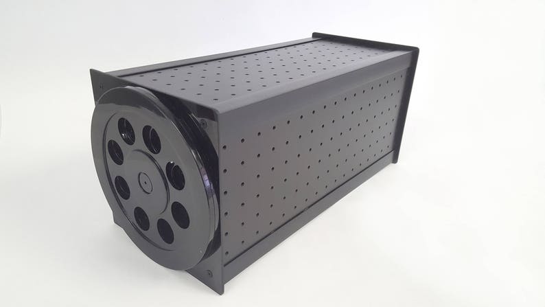 May include: Black storage box with a round, perforated lid. The lid has a series of holes around the edge.