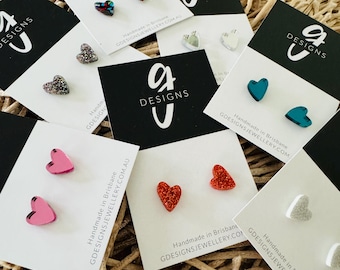 Pode incluir: Conjunto de brincos em forma de coração em várias cores e acabamentos, incluindo glitter, vermelho, rosa, azul-turquesa e prata. Os brincos são exibidos em pequenos cartões com o texto "G Designs" e "Handmade in Brisbane, GDesignsJewellery.com.au".