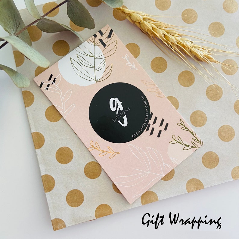 Puede incluir: Una tarjeta de visita con el logo "gJ Designs" sobre un fondo rosa con dise&ntilde;os de hojas y abstractos. La tarjeta est&aacute; sobre papel de regalo de lunares, con espigas de trigo y eucalipto.