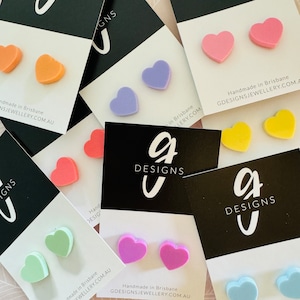 May include: Assortment of colourful heart-shaped earrings made of polymer clay. The earrings are displayed on white and black cards with the text "G Designs" and "Handmade in Brisbane, GDesignsJewellery.com.au".