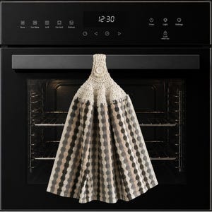 May include: A hanging kitchen towel featuring a cream-coloured crocheted top with a single button closure. The towel body displays a vertical striped pattern in alternating shades of dark grey, light grey, and cream, creating a textured appearance.