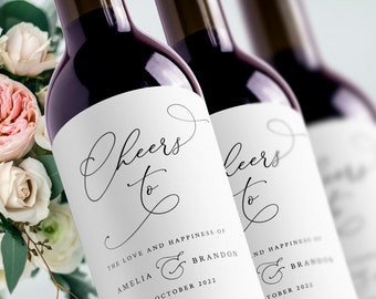 Könnte beinhalten: Zwei weiße Weinflaschenetiketten mit schwarzer Kalligraphie, die "Cheers to" gefolgt von den Namen Amelia & Brandon und Oktober 2022 lautet.