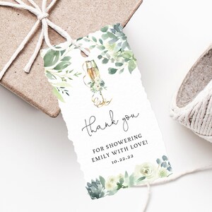 May include: A white thank you tag with green and white floral illustrations and a gold champagne glass. The text reads "Thank you for showering Emily with love! 10.22.22"