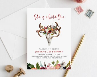 May include: A white invitation card with the text "She is a Wild One" in red script. The card features a watercolor illustration of a skull with antlers and floral accents. Additional text provides event details.