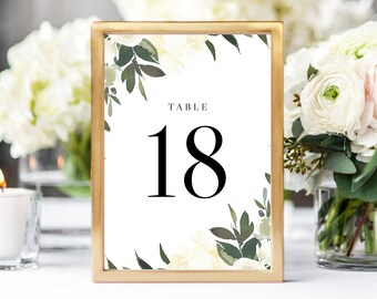 May include: Gold frame table number card with white floral design and black text that reads "TABLE 18".