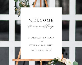 May include: White wedding welcome sign with black text. The sign reads "Welcome to our wedding" in cursive script, followed by "Morgan Taylor and Ethan Wright" and "October 22, 2022".