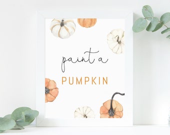 May include: A framed print featuring watercolor pumpkins in shades of orange and white against a white background. The text "paint a PUMPKIN" is written in black and orange script. Eucalyptus sprigs are in the background.