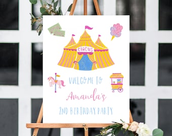 May include: A white sign with a circus theme for a 2nd birthday party. The sign features a yellow and pink striped tent with a blue star pattern, a carousel horse, a popcorn stand, and cotton candy. The text on the sign reads "Welcome to Amanda's 2nd Birthday Party".
