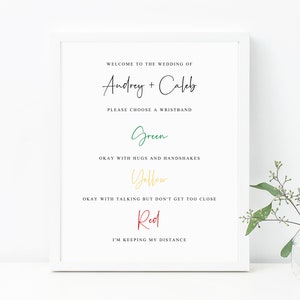 May include: A white sign with black text that reads "Welcome to the wedding of Andrey + Caleb. Please choose a wristband."  The sign has three colored options: green, yellow, and red.  Green means okay with hugs and handshakes, yellow means okay with talking but don't get too close, and red means I'm keeping my distance.