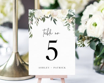 May include: White floral wedding table number card with the text "table no. 5" and the names "Ashley + Patrick" printed below.