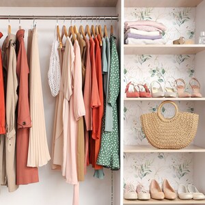 May include: A closet with a variety of clothing hanging on hangers. The clothing includes a long red coat, a long white skirt, a pink dress, a brown dress, a red dress, a green dress, and a white dress. The closet also has shelves with a straw bag, shoes, and other items.