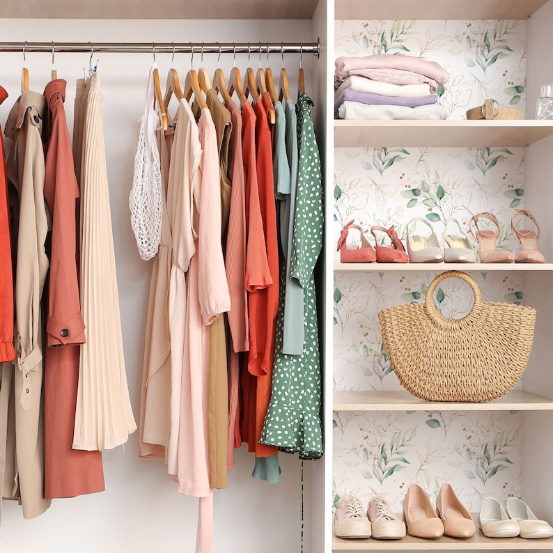 May include: A closet with a variety of clothing hanging on hangers. The clothing includes a long red coat, a long white skirt, a pink dress, a brown dress, a red dress, a green dress, and a white dress. The closet also has shelves with a straw bag, shoes, and other items.